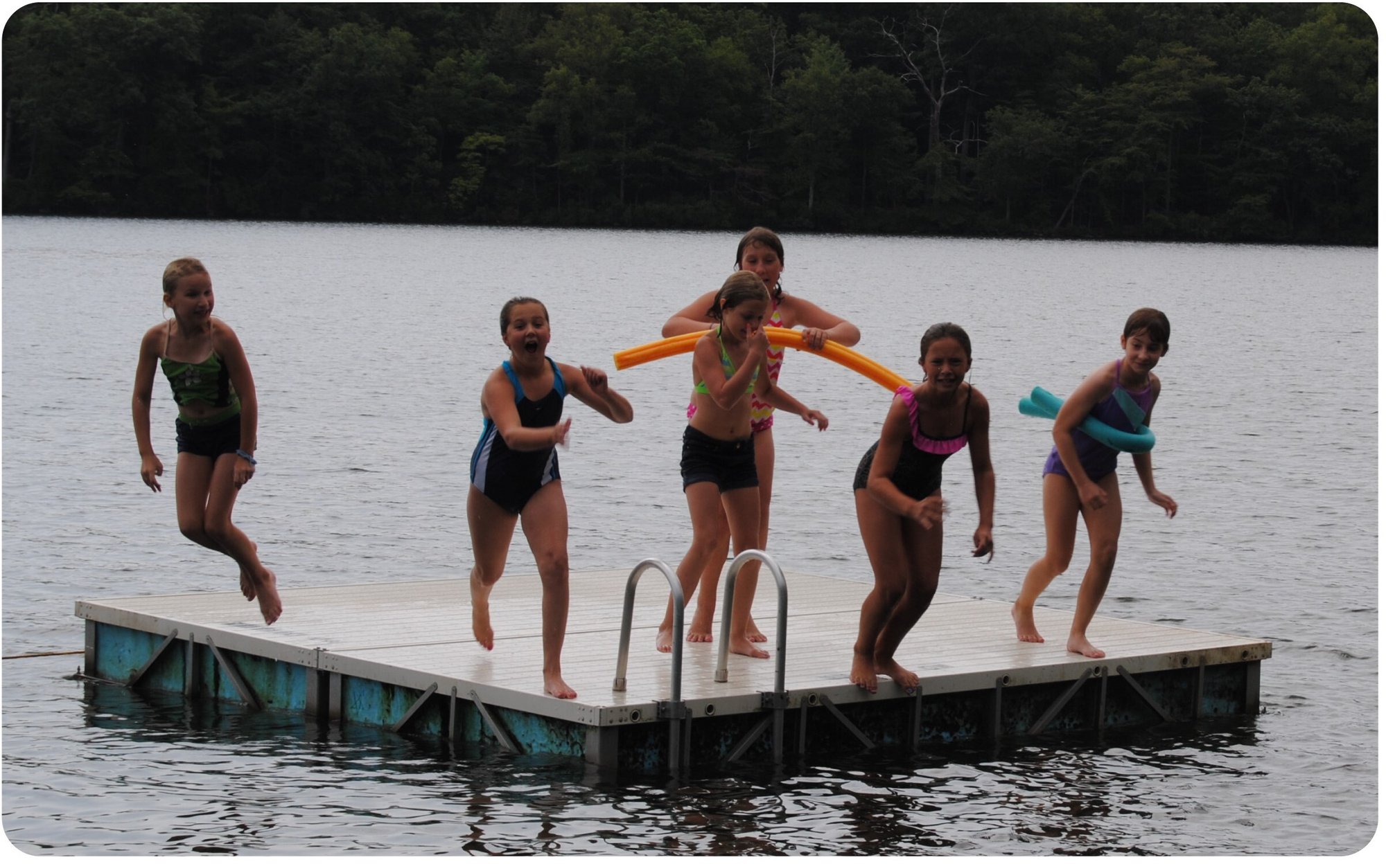 Swimmers leap off the dock into the lake at day camp